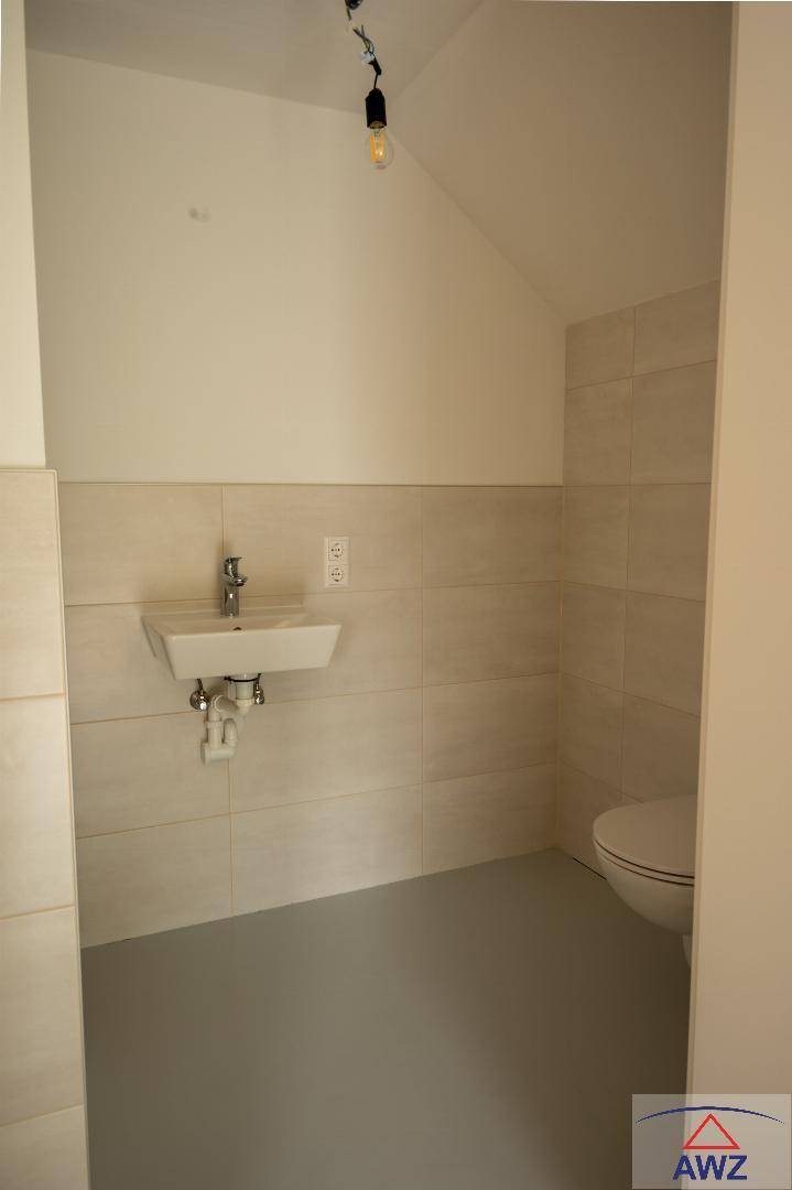 Kleines WC mit Wand-WC, Einzelwaschbecken und hellen Fliesen im unteren Bereich.