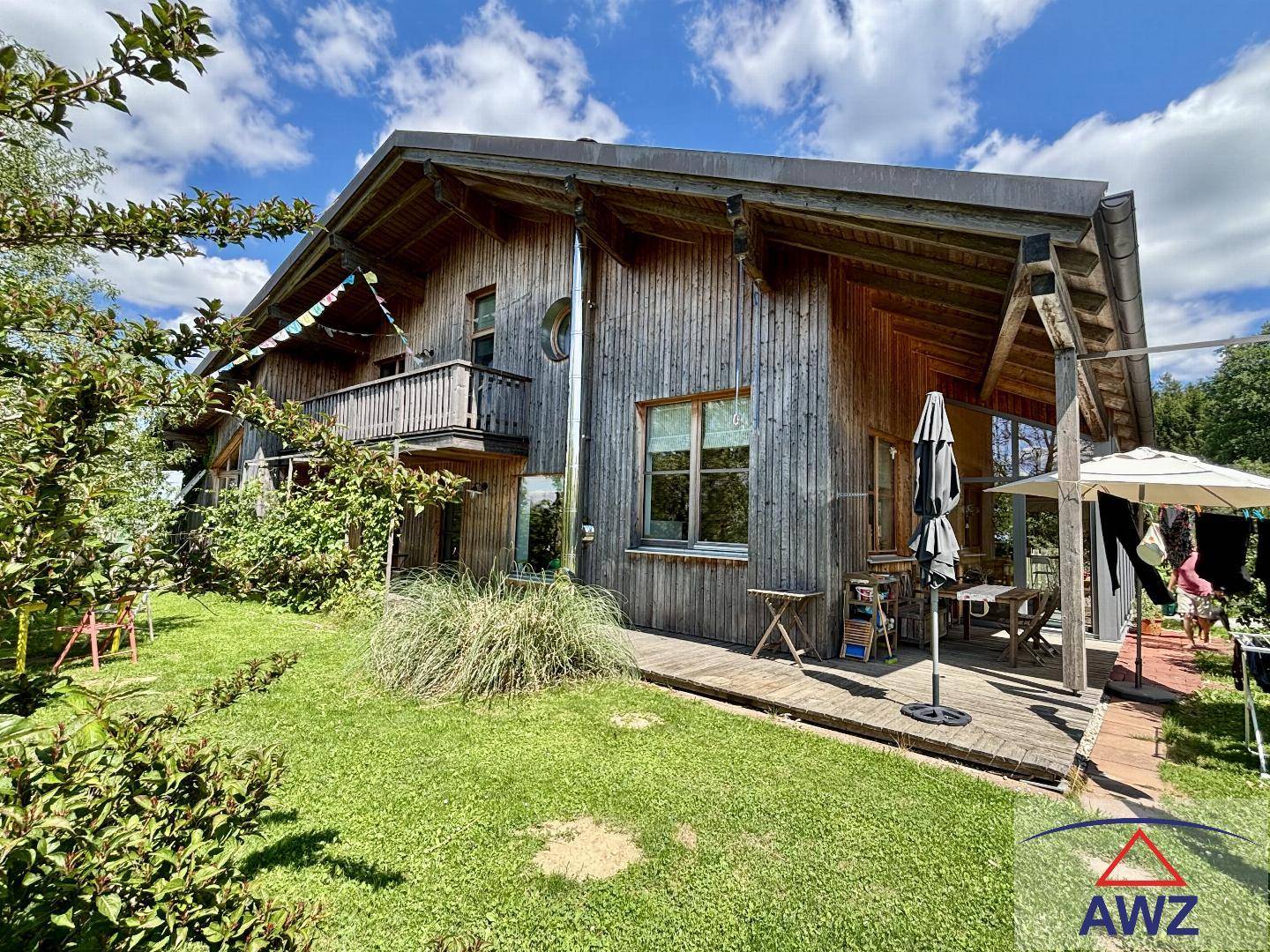 Holzhaus mit großer Rasenfläche und einer gemütlichen Terrasse mit Sonnenschirmen im Grünen.