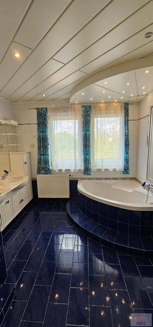 Badezimmer mit dunkelblauen Fliesen, Eckbadewanne, Einzelwaschbecken und Fenster mit Vorhängen.