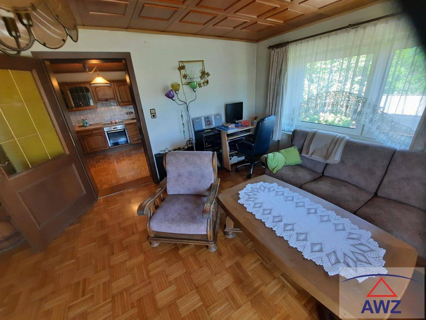 Wohnzimmer mit Holzkassettendecke, Parkett und offenem Zugang zur Küche.