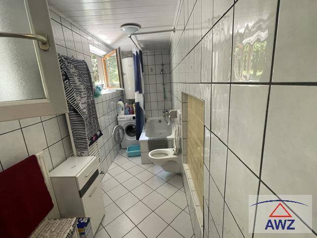 Gefliestes Badezimmer mit WC, Waschbecken, Waschmaschine und Fenster für Tageslicht.