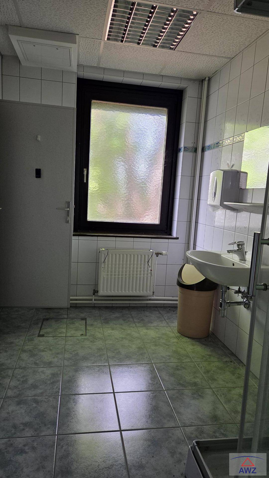 Badezimmer mit Waschbecken, Fenster und grauen Fliesen an Boden und Wänden.