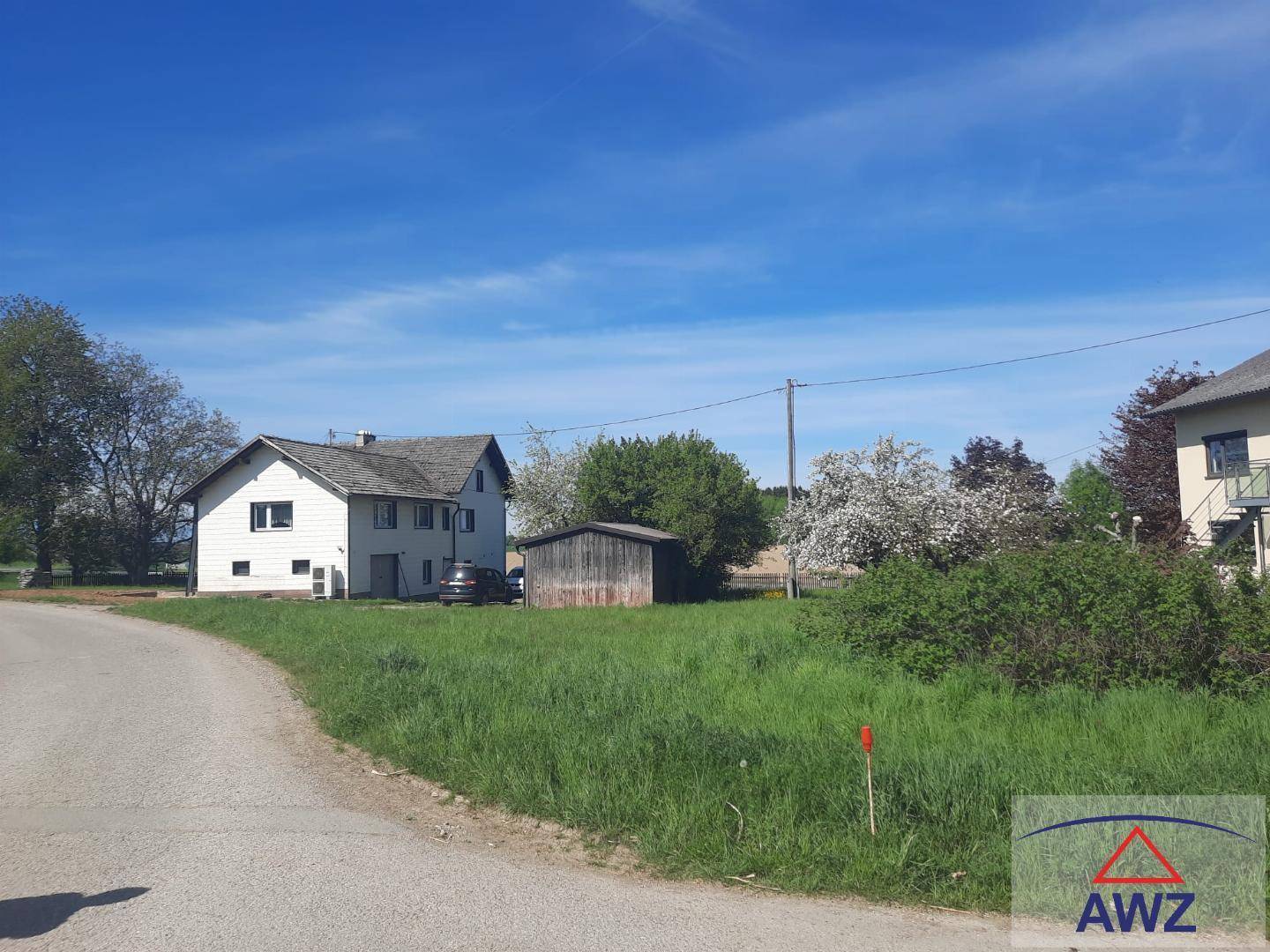 Haus in ländlicher Umgebung mit großem Rasen und Nebengebäude unter blauem Himmel.