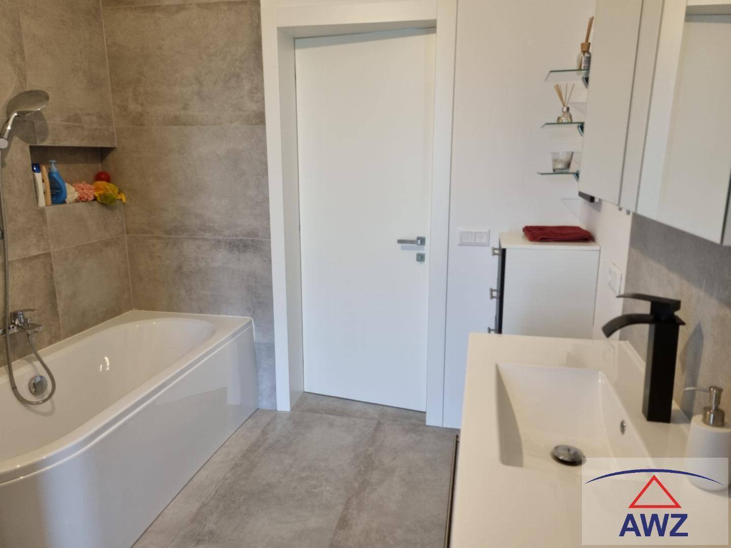 Modernes Badezimmer mit Badewanne, Waschbecken und grauen Fliesen an Wänden und Boden.