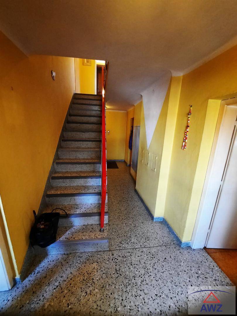 Heller Flur mit Treppe, gelben Wänden und Terrazzo-ähnlichem Bodenbelag.
