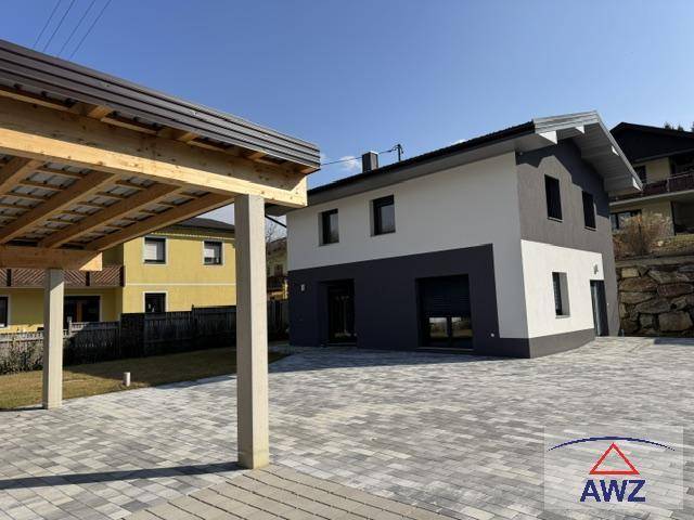 Modernes Einfamilienhaus mit Carport und gepflastertem Vorplatz unter blauem Himmel.