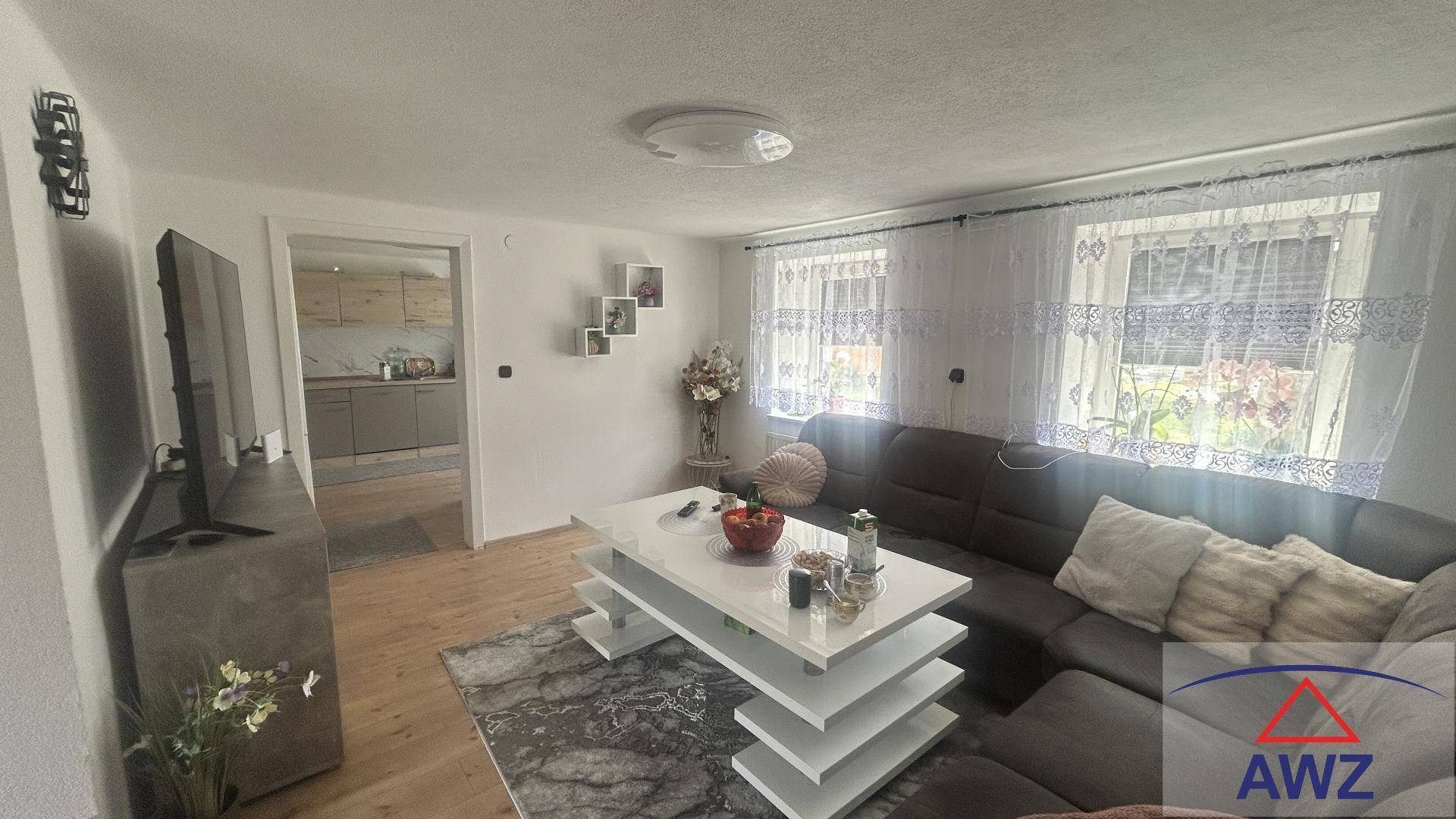 Helles Wohnzimmer mit bequemer Couch, Couchtisch und Zugang zu einer angrenzenden Küche.