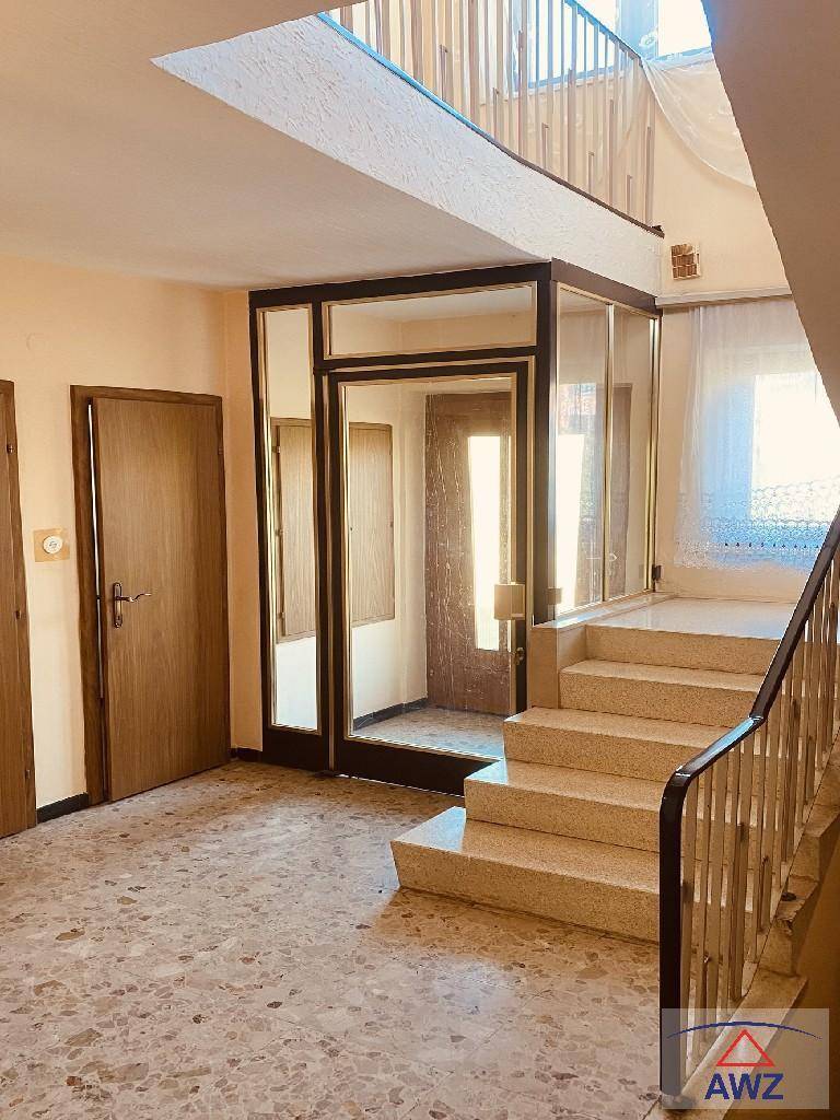 Heller Eingangsbereich mit Marmorboden, Treppe und einem kleinen verglasten Aufzug.