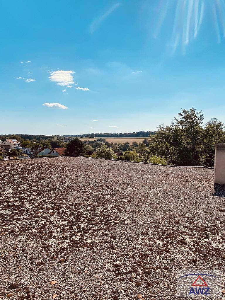 Flachdach mit Kiesbelag und weitem Blick über die umliegende Landschaft und ein Dorf.