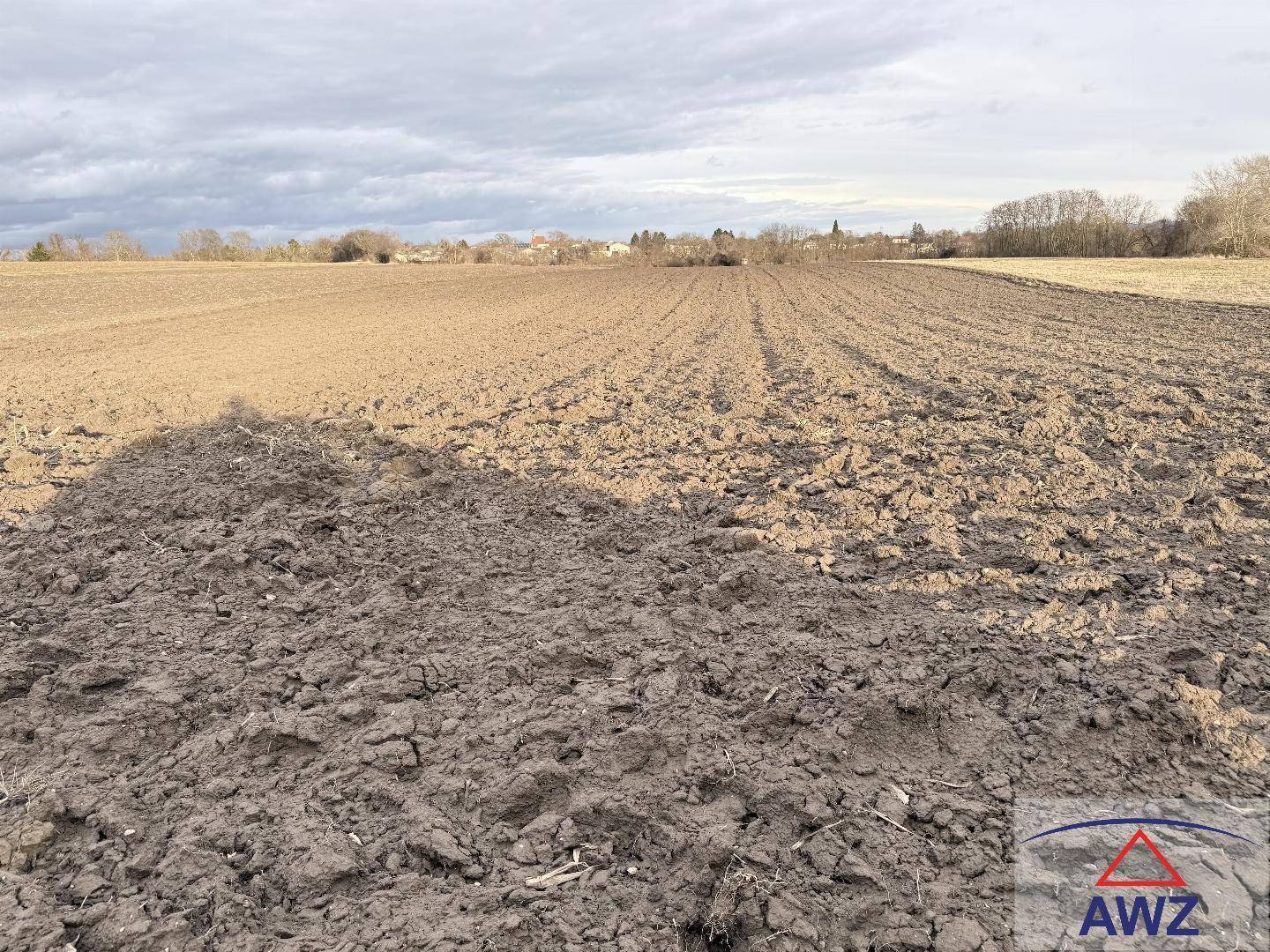 Ausgedehntes Ackerland mit Blick auf die ländliche Umgebung und einen bewölkten Himmel.
