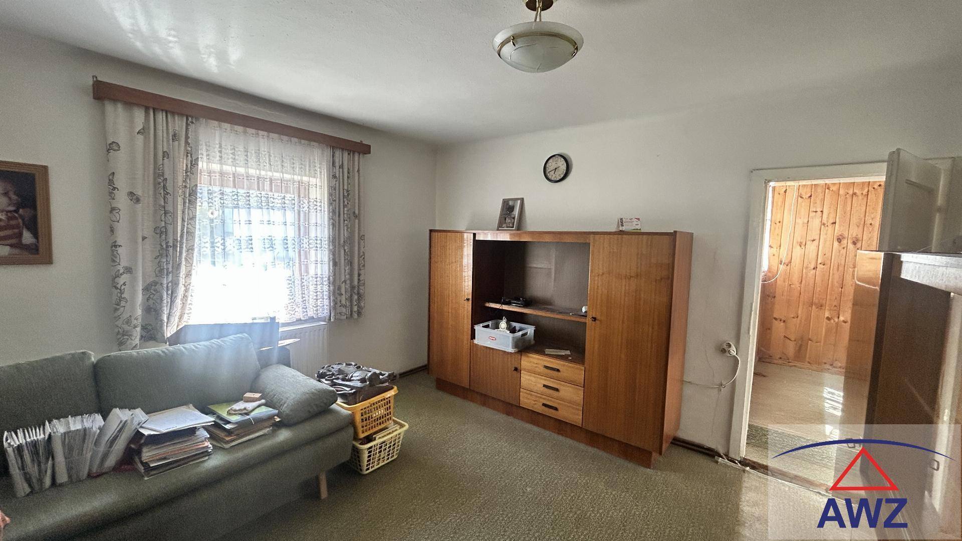 Gemütliches Wohnzimmer mit Sofa, Holzschrank und Blick durch das Fenster ins Grüne.