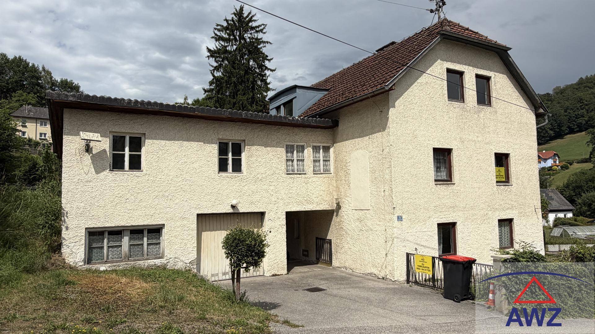 Vorderansicht des Hauses mit Garage, gepflasterter Einfahrt und Blick auf die umliegende grüne Landschaft.