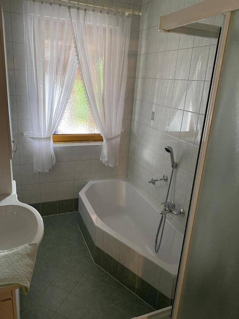 Badezimmer mit Badewanne, Duschvorrichtung, Fliesen und einem Fenster für Tageslicht.