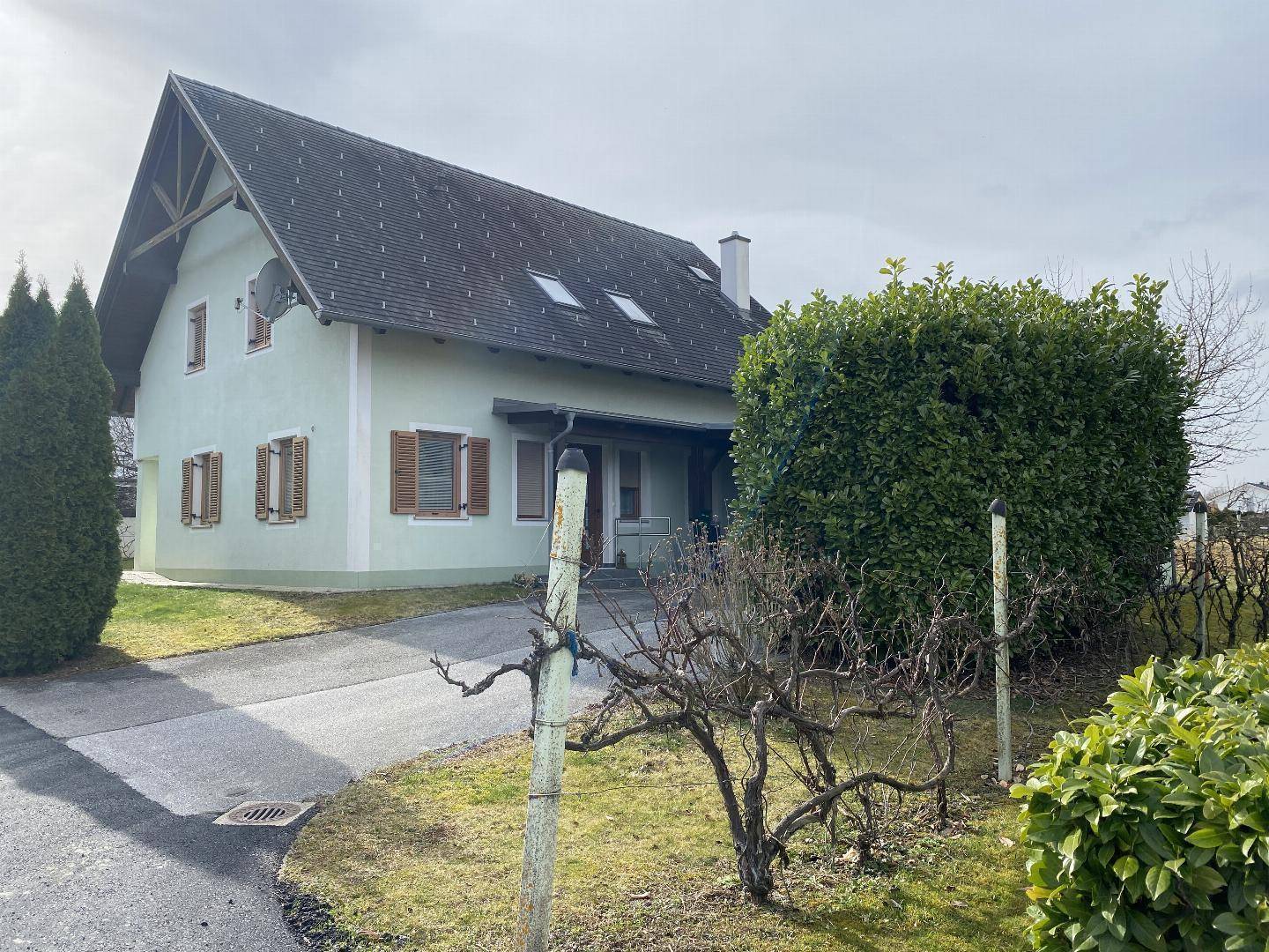 Einfamilienhaus mit Satteldach, grüner Fassade, Fensterläden und gepflegtem Vorgarten.