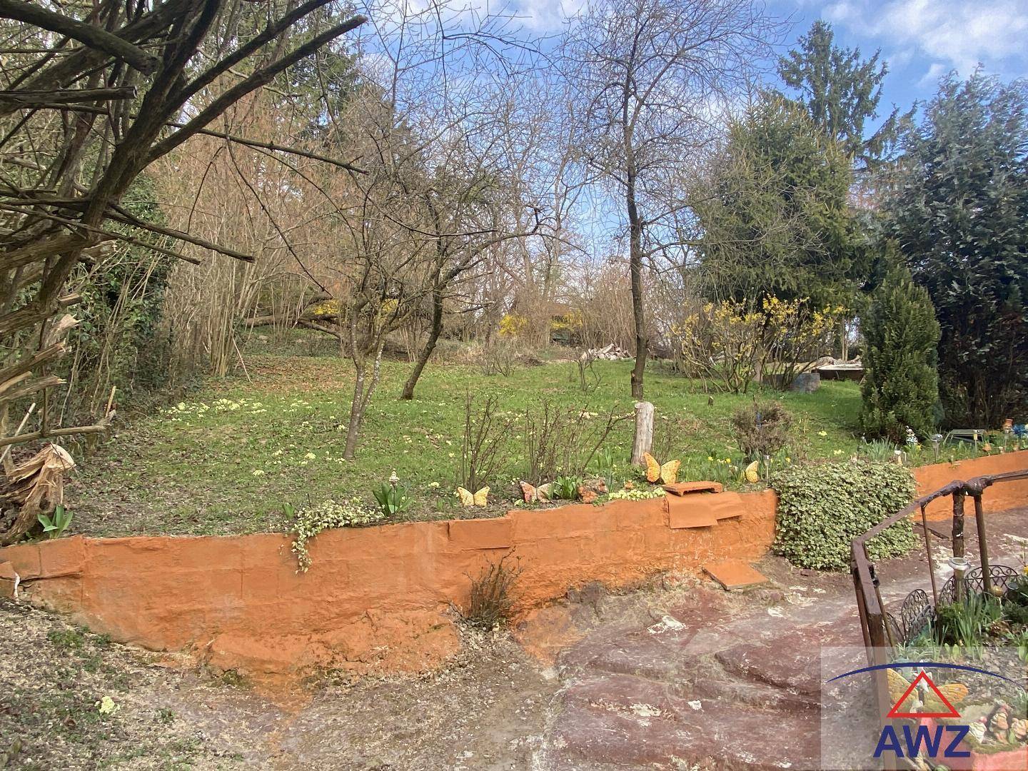 Gepflegter Gartenbereich mit Rasenfläche, Bäumen und einer niedrigen orangefarbenen Mauer.