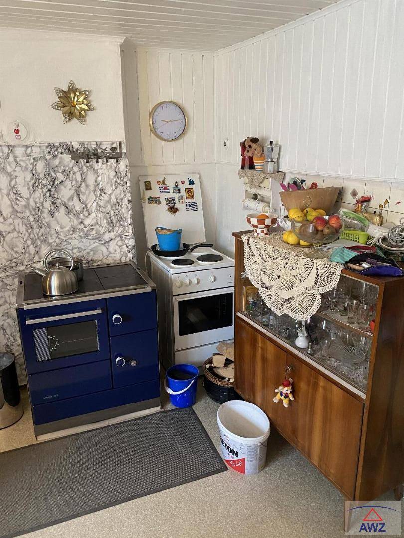 Rustikale Küche mit blauem Holzofen, weißem Elektroherd und traditionellem Holzschrank.