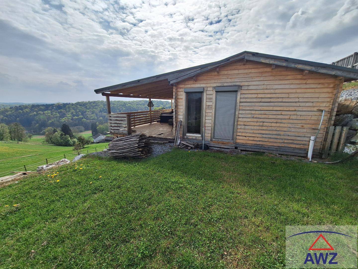 Kleine Holzhütte mit überdachter Terrasse und weitem Blick über grüne Hügel und Wälder.
