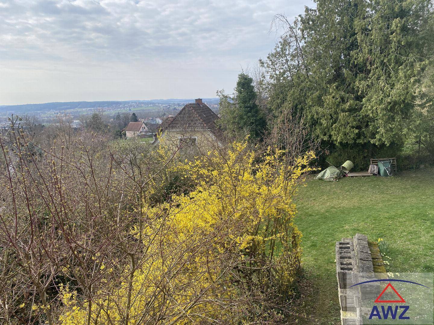 Großer Garten mit blühenden Sträuchern und weitem Blick über die Landschaft und Häuser.