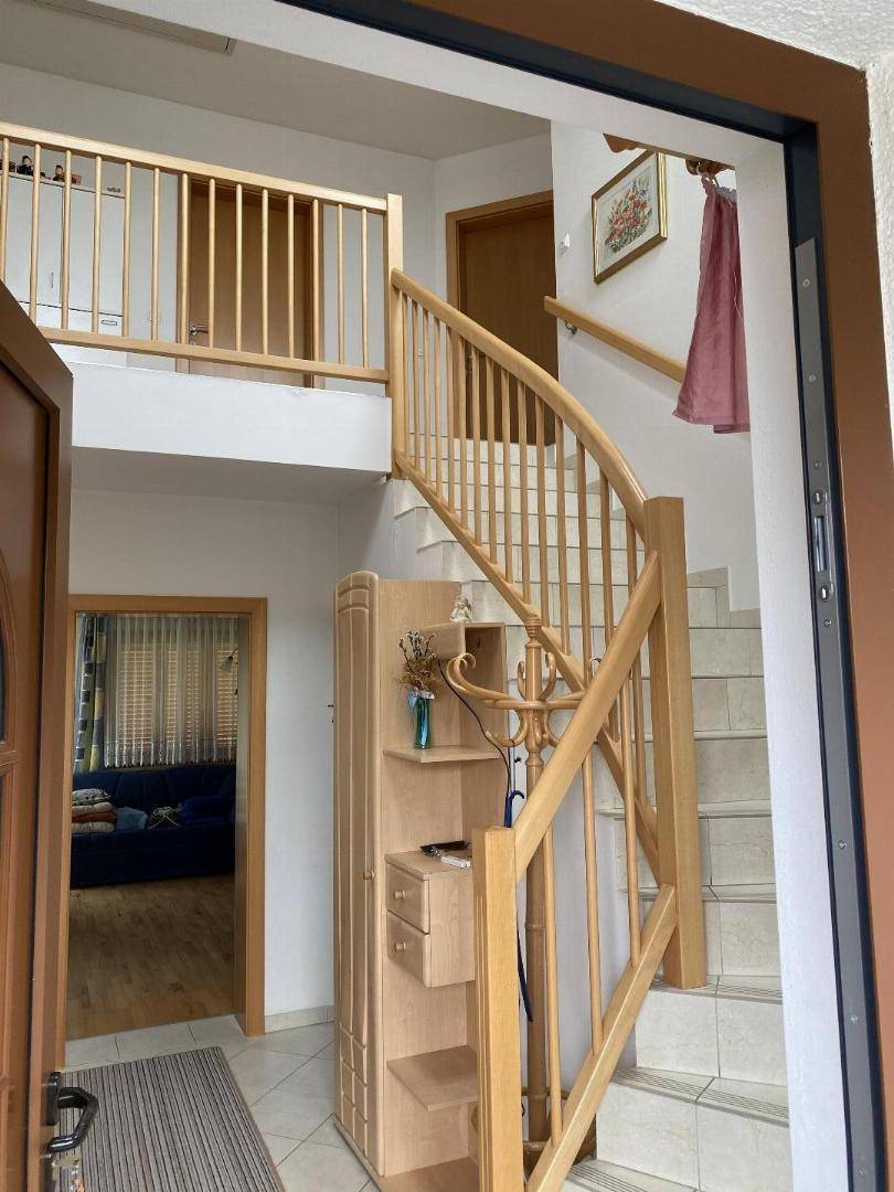 Heller Eingangsbereich mit offener Holztreppe, Galerie und Fliesenboden im Erdgeschoss.