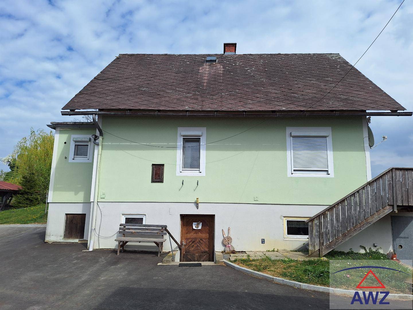 Wohnhaus mit hellgrüner Fassade, braunem Dach und einer externen Holztreppe im ländlichen Stil.