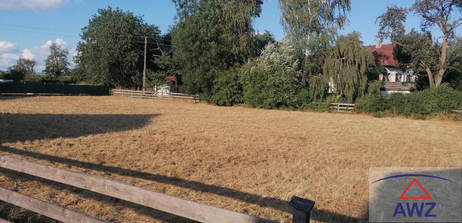 Weitläufiges Baugrundstück mit Holzzaun und Bäumen im Hintergrund unter blauem Himmel.