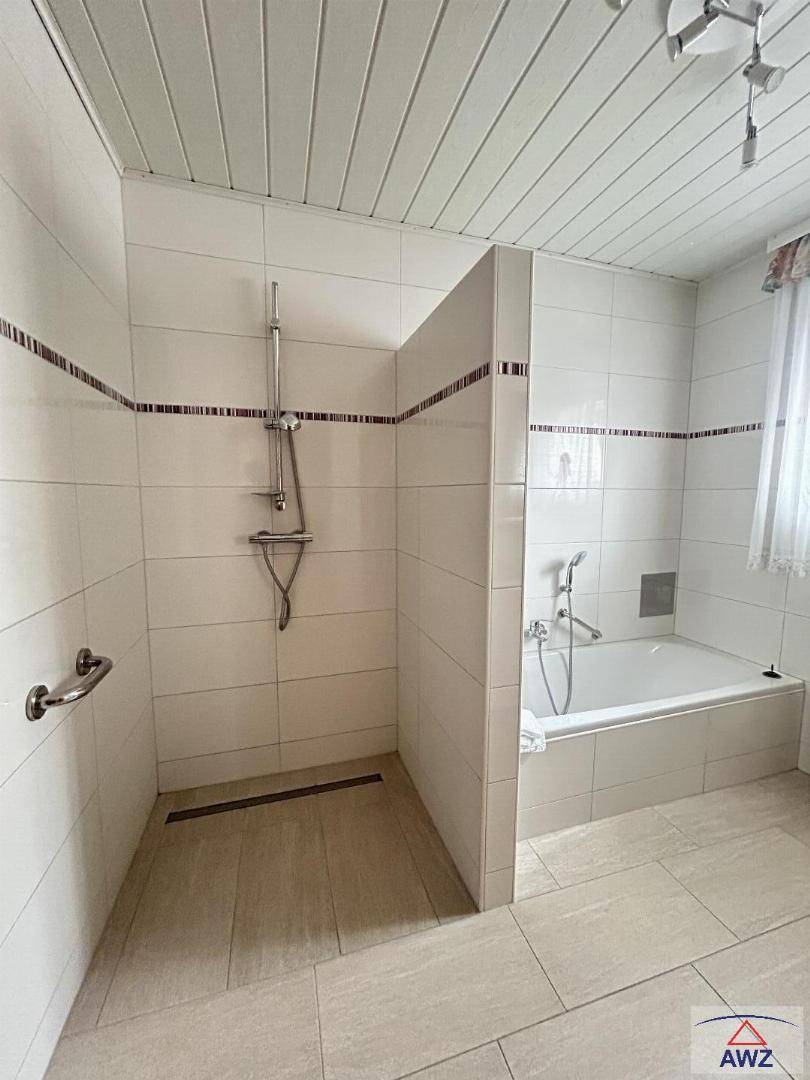 Badezimmer mit begehbarer Dusche, Badewanne und Haltegriffen, ausgestattet mit hellen Fliesen.