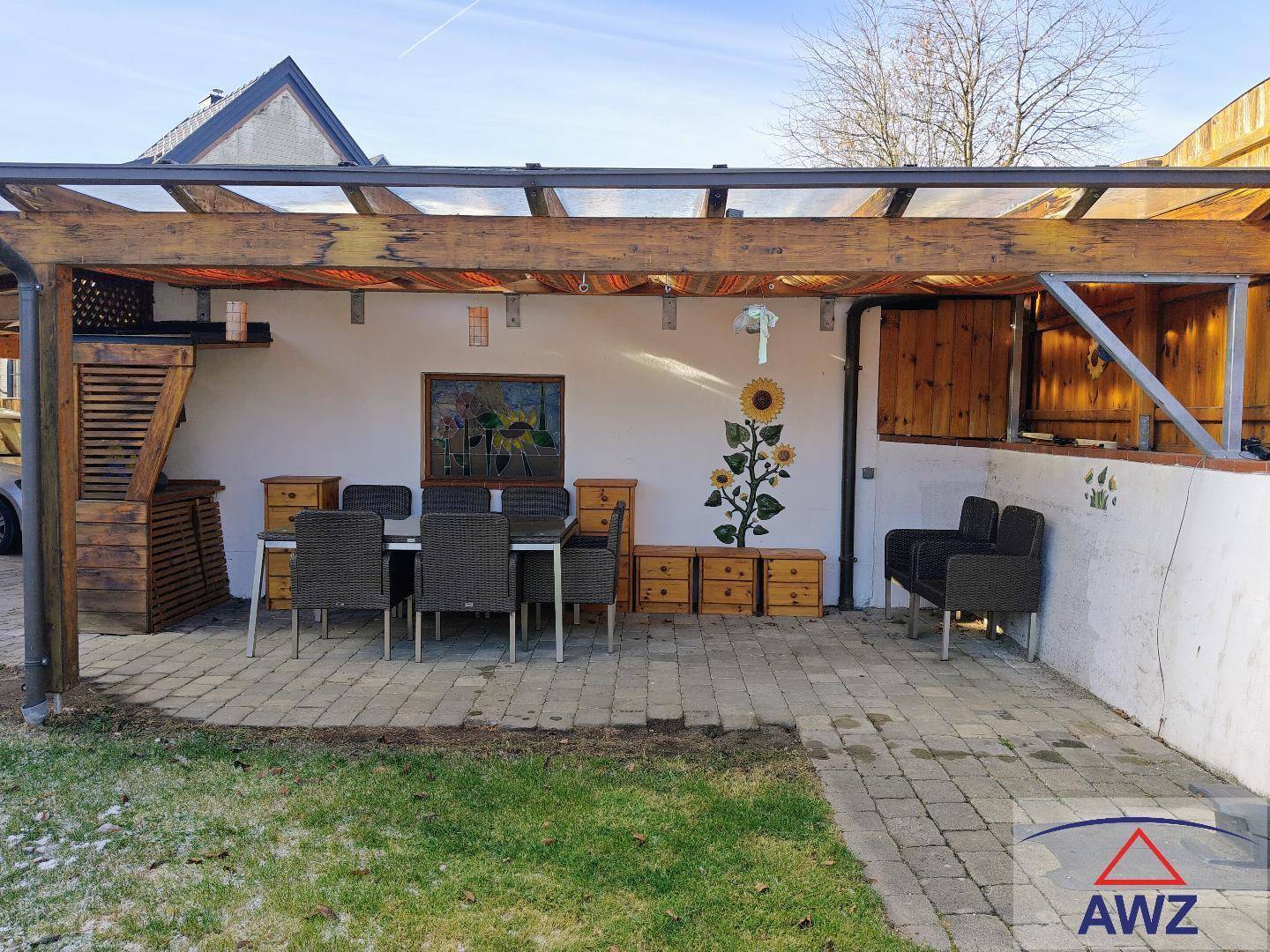 Gemütliche Außenterrasse mit Pergola, Esstisch und dekorativen Sonnenblumen an der Wand.