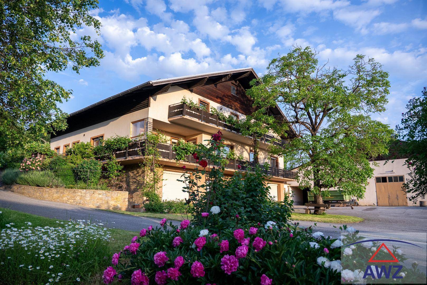 Charmantes Wohnhaus mit mehreren Balkonen, umgeben von blühenden Blumen und Bäumen.