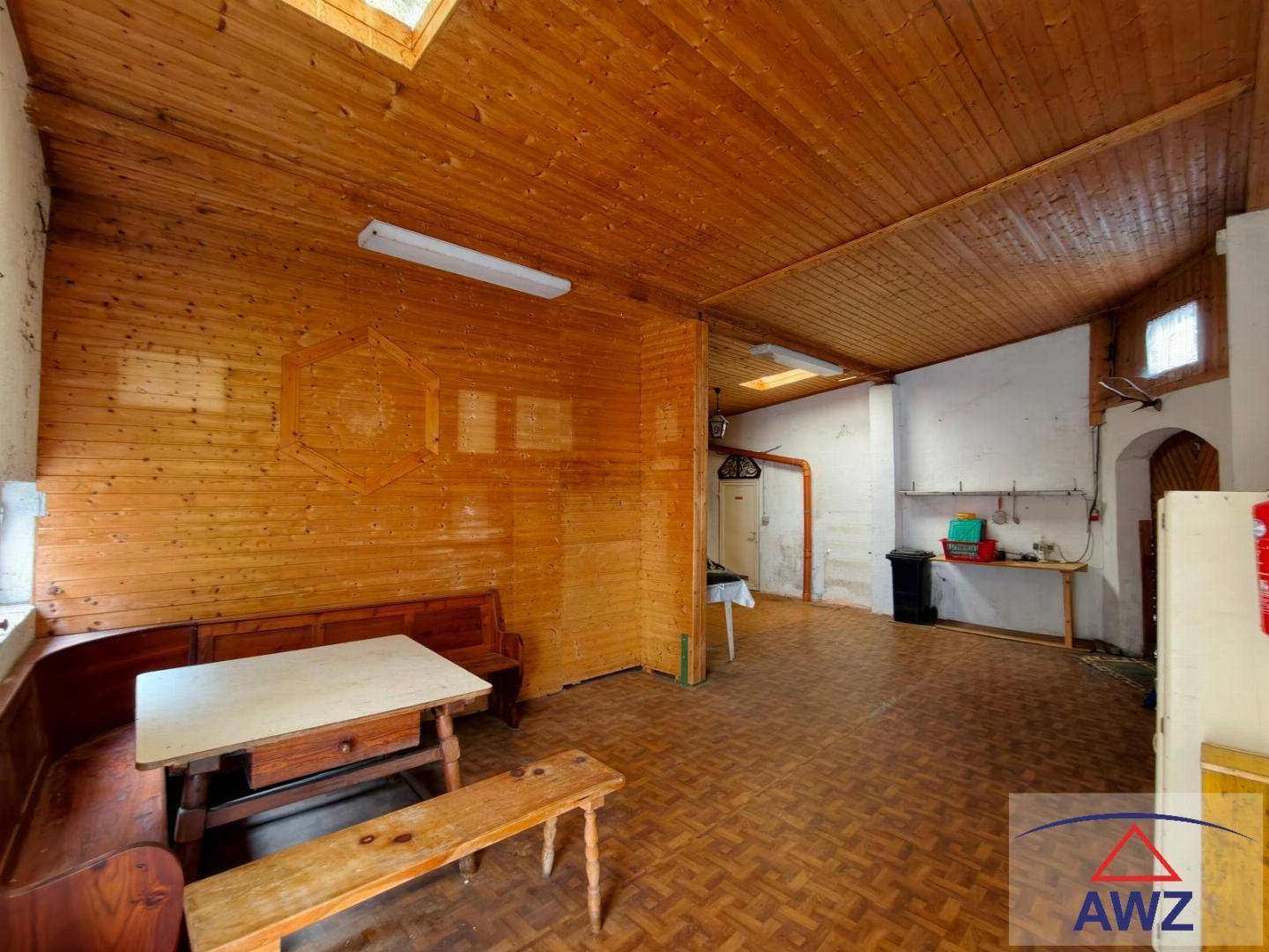 Rustikaler Raum mit Holzvertäfelung, Holzbalkendecke und einfacher Sitzgelegenheit, beleuchtet durch Dachfenster.