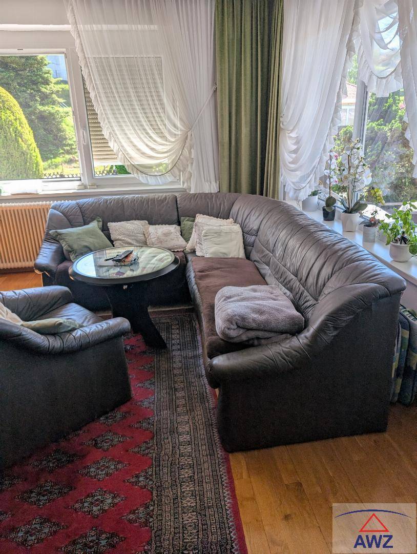 Gemütliches Wohnzimmer mit großem Ecksofa, Holzboden und viel Tageslicht durch die Fenster.