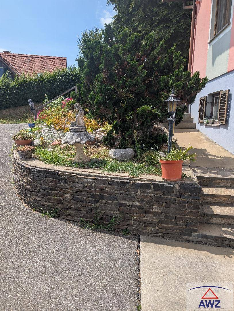 Eingangsbereich des Hauses mit Steintreppe, dekorativer Mauer und bepflanzten Blumenbeeten.