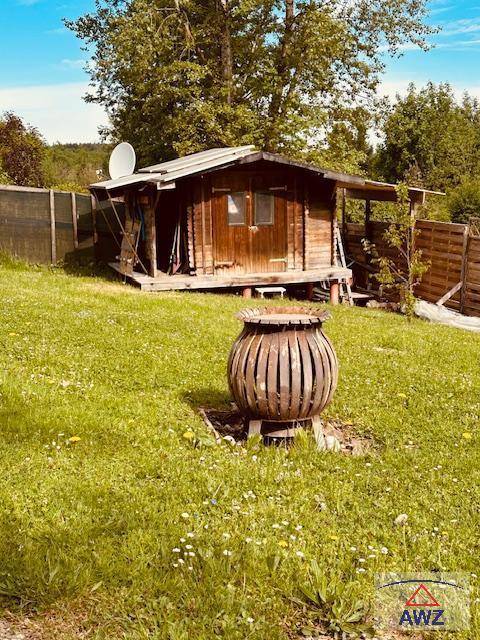 Rustikale Holzhütte auf Stelzen im Grünen mit einer dekorativen Feuerstelle im Vordergrund.
