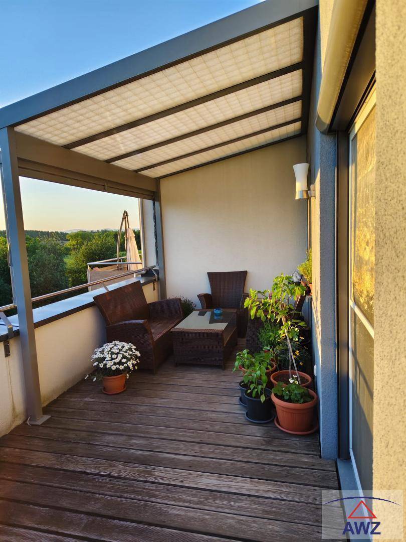 Geräumiger Balkon mit Holzdielen, bequemen Sitzgelegenheiten und weitem Blick ins Grüne, perfekt für den Abend.