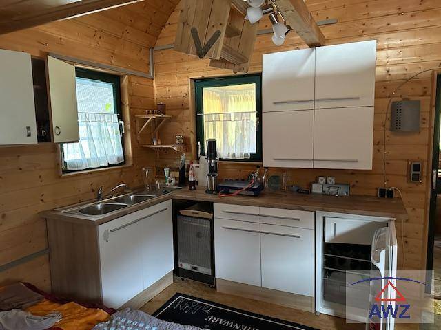 Kleine Küche in einer Holzhütte mit weißen Schränken, Spüle und Holzvertäfelung.