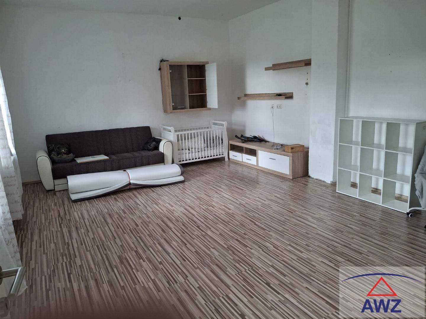 Heller Wohnbereich mit Sofa, Babybett und Regalen, ideal für Familienleben.