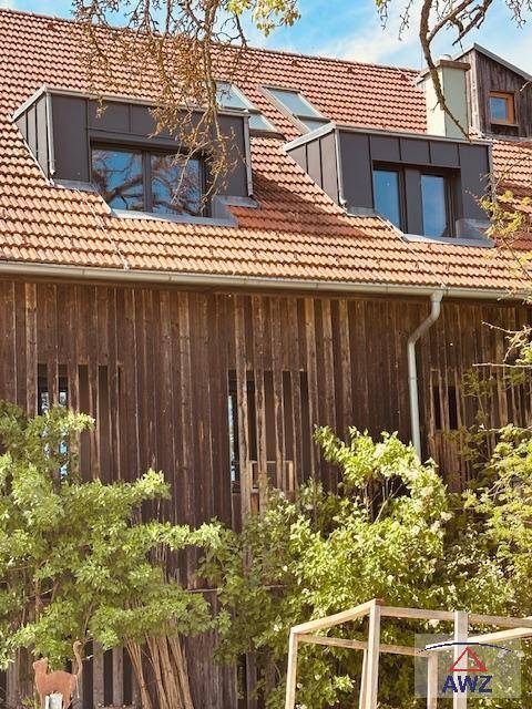 Rustikale Holzfassade eines Gebäudes mit Ziegeldach und modernen Dachgauben, umgeben von Bäumen.