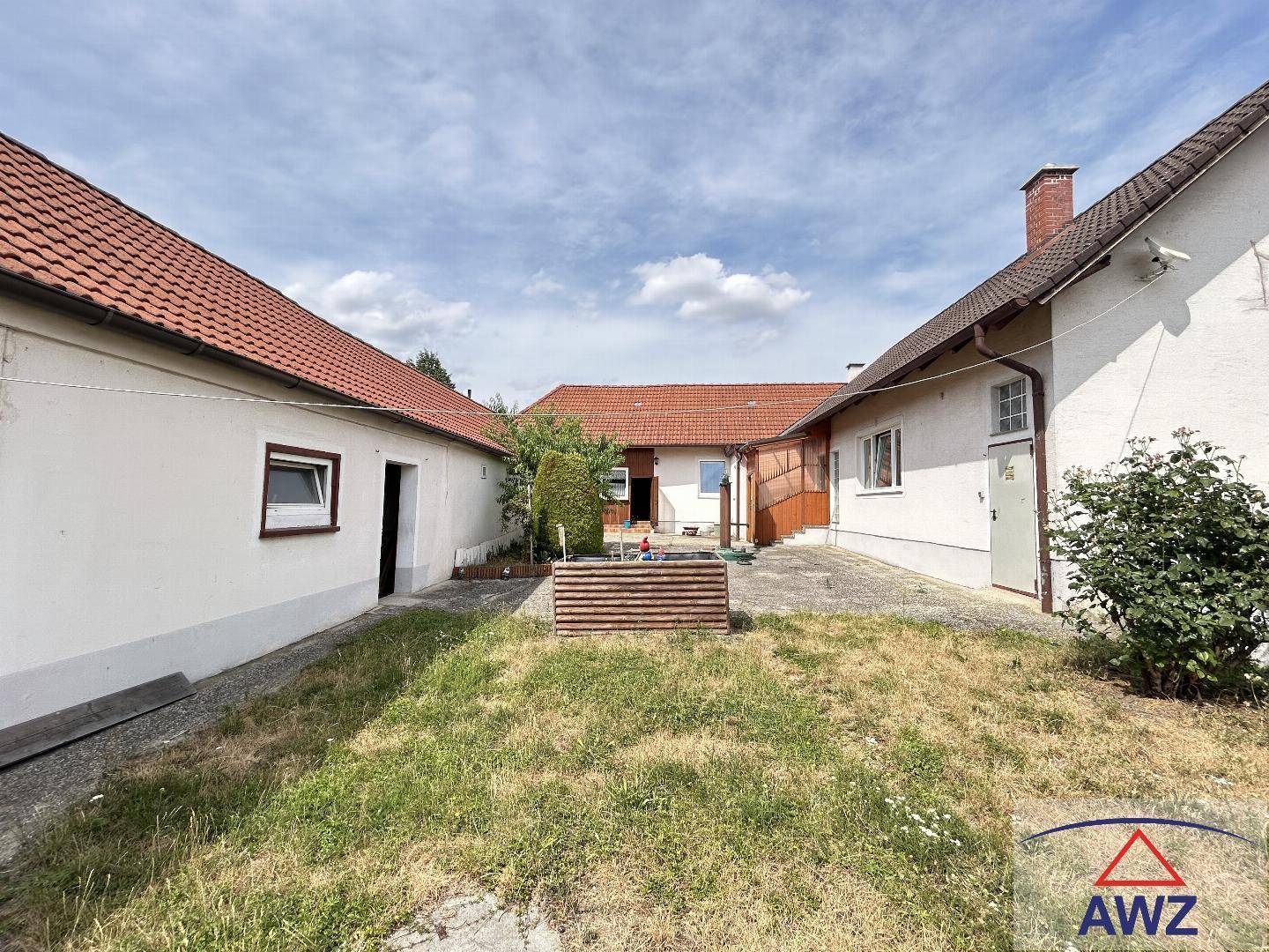 Innenhof mit Rasenfläche und gepflastertem Bereich, umgeben von Gebäuden mit Ziegeldächern.