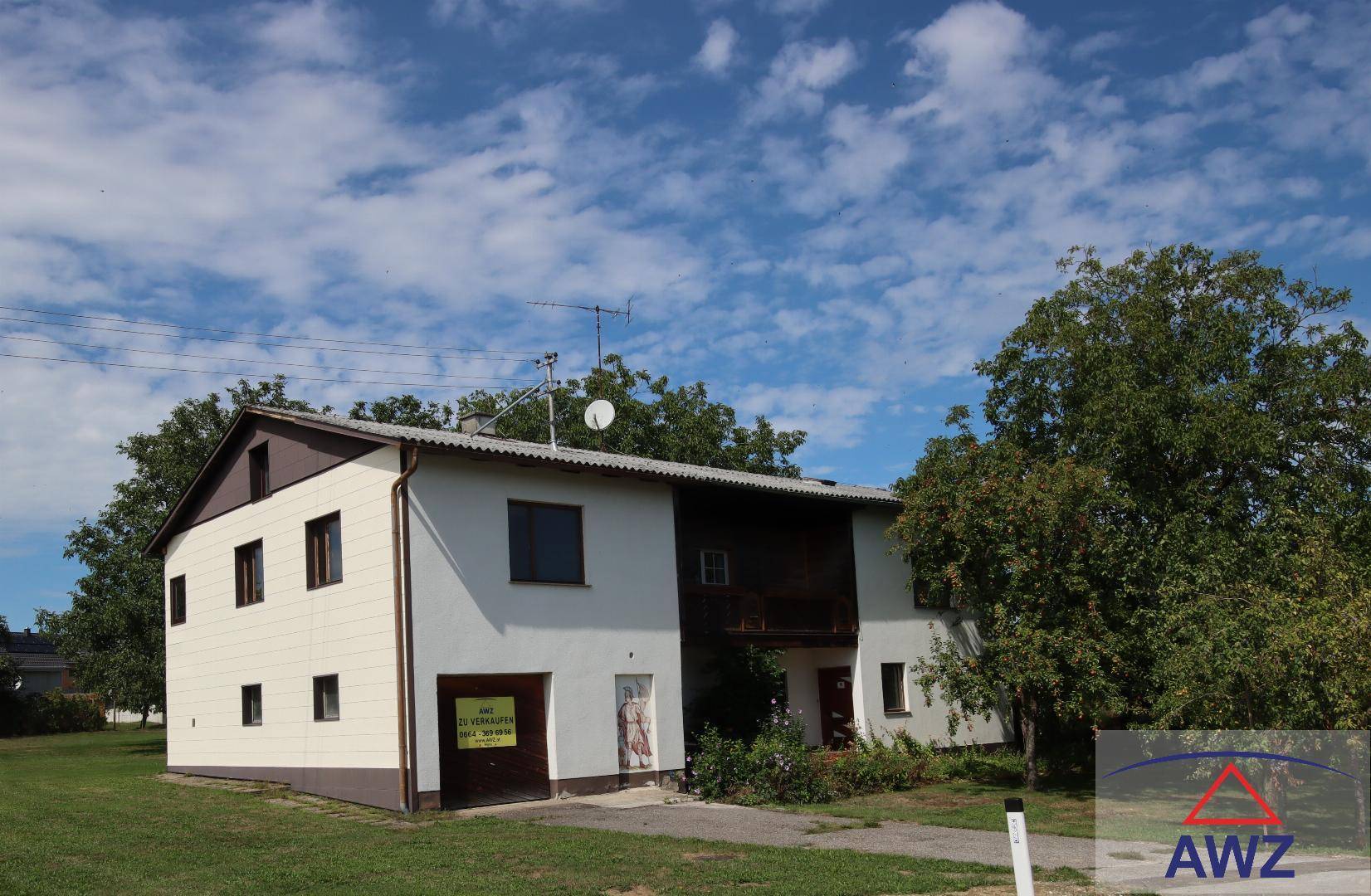 Vorderansicht des Hauses mit Einfahrt und 'Zu verkaufen'-Schild im ländlichen Umfeld.