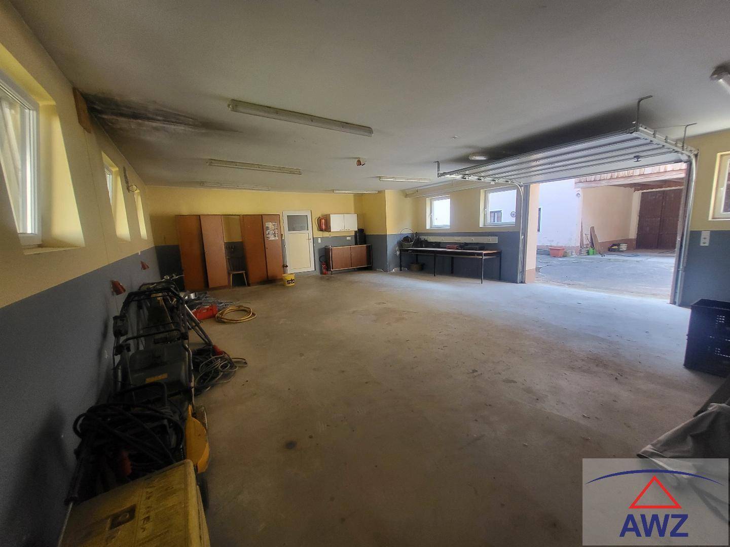 Geräumige Garage oder Werkstatt mit Betonboden und offenem Garagentor.