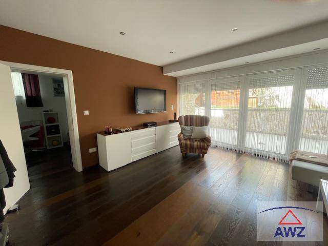 Gemütliches Wohnzimmer mit dunklem Holzboden, großen Fenstern und Zugang zum Außenbereich.