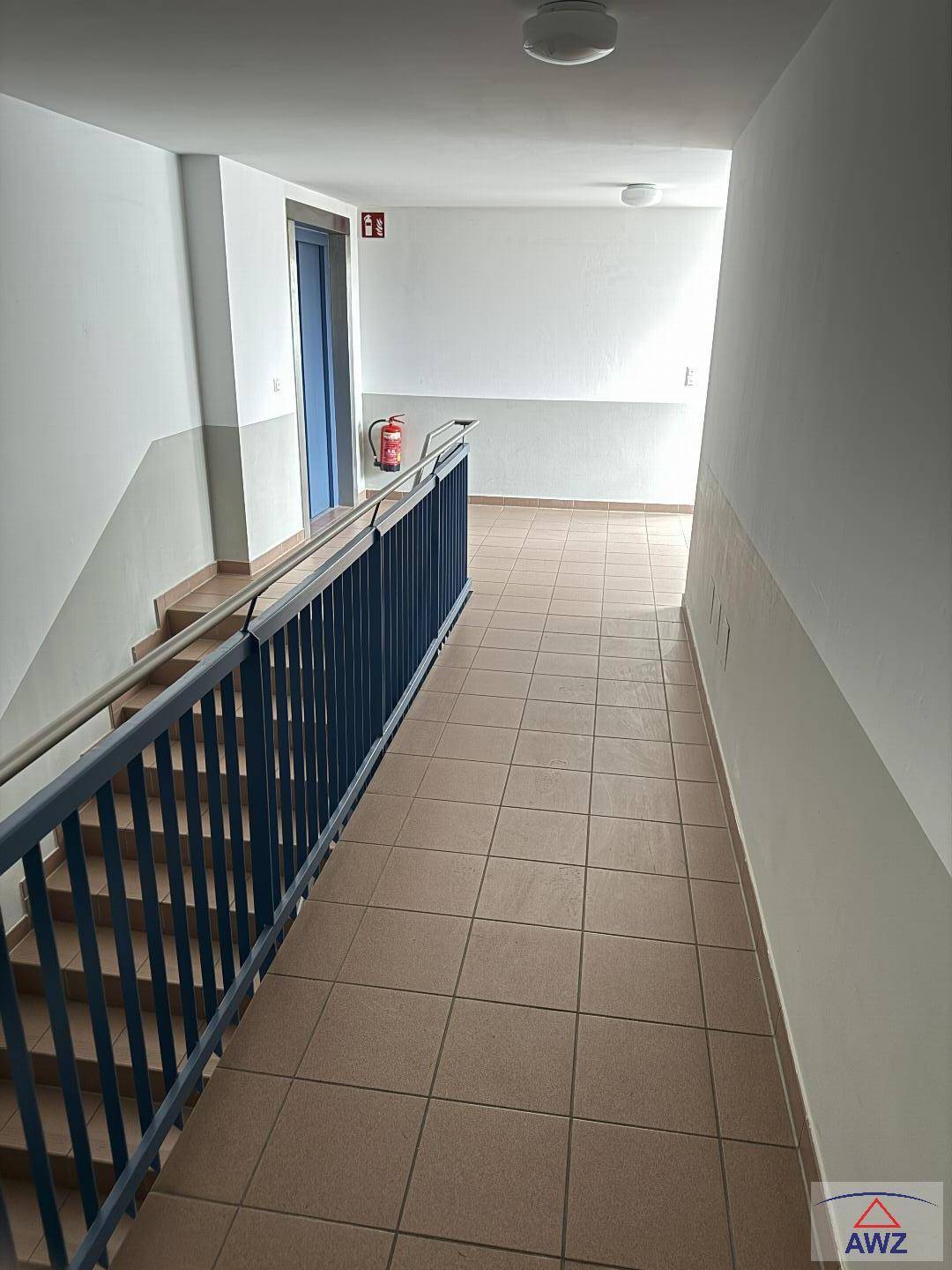 Heller Treppenhausbereich mit Fliesenboden und blauem Geländer im Mehrfamilienhaus.