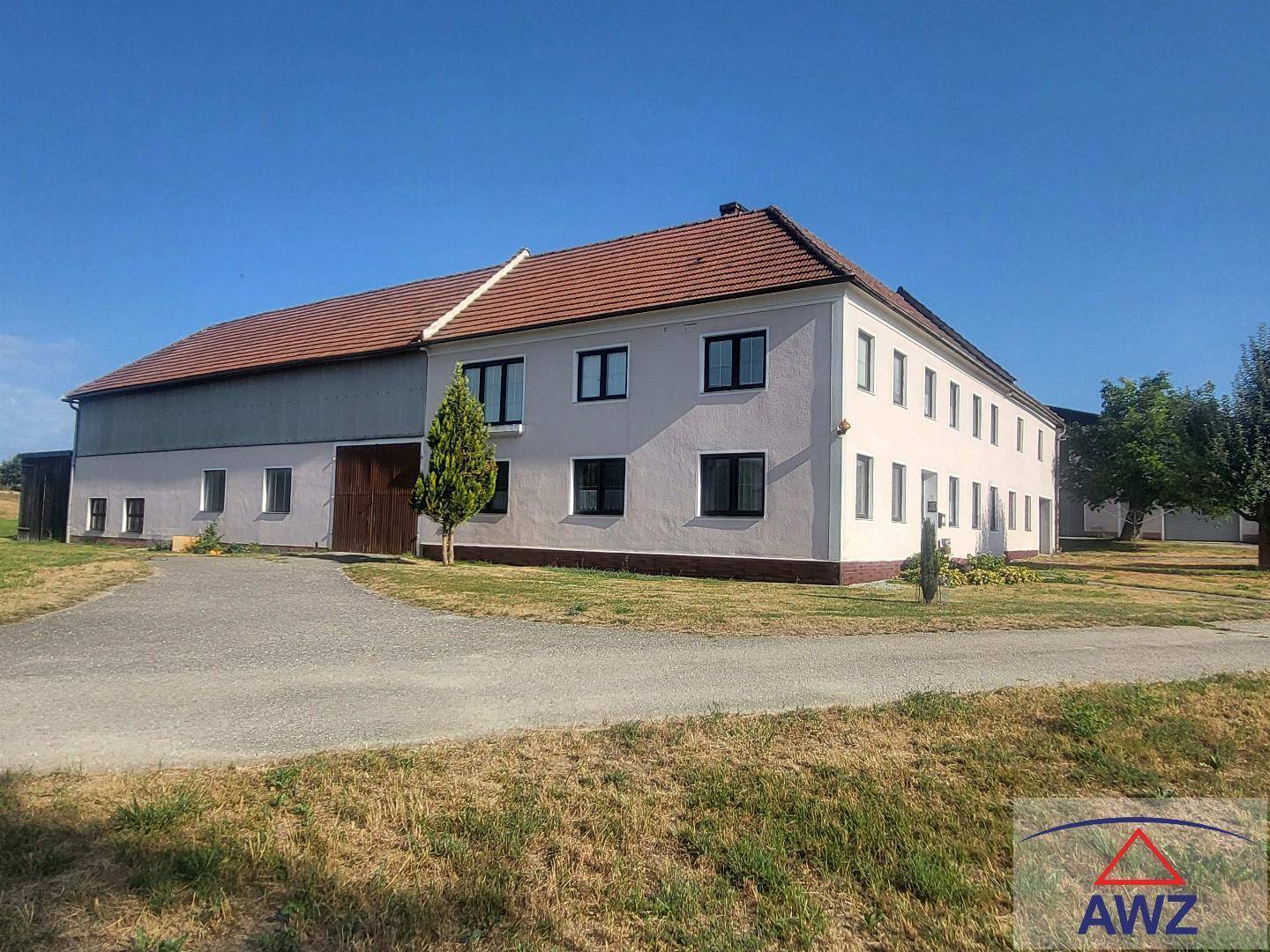 Großes Bauernhaus mit heller Fassade und rotem Ziegeldach, umgeben von einer weiten Zufahrt.