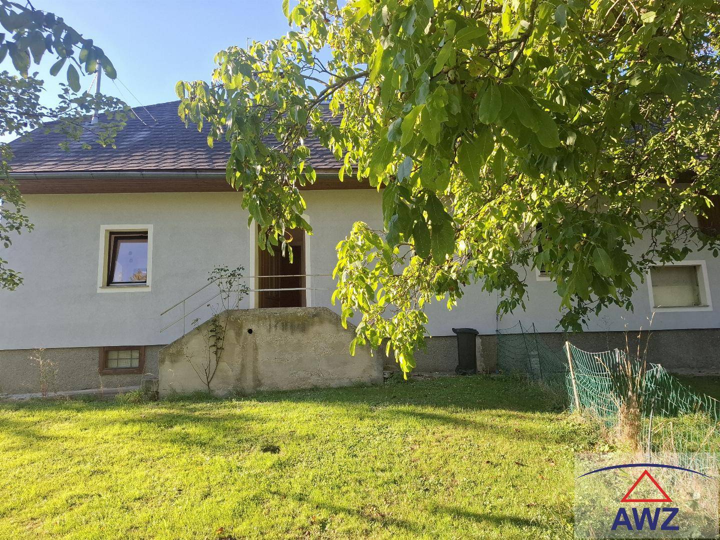 Vorderansicht des Hauses mit grünem Rasen und Bäumen, umgeben von ländlicher Natur.