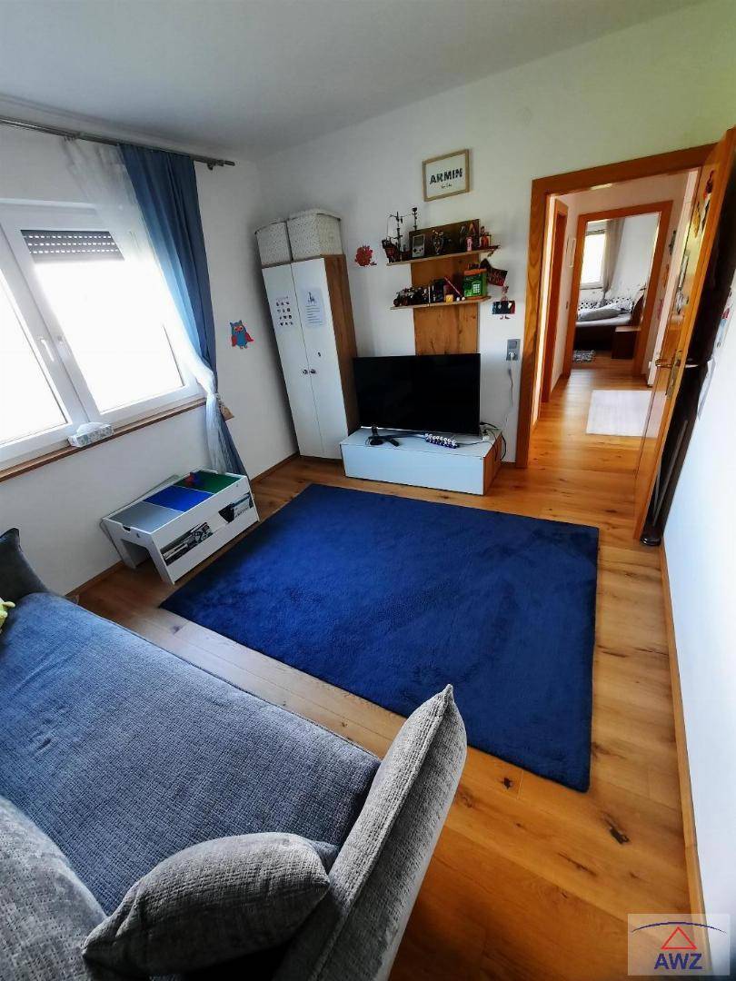 Helles Schlafzimmer mit Holzboden, blauem Teppich und einem Fenster, das Tageslicht hereinlässt.