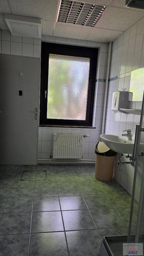 Badezimmer mit Fliesenboden, Waschbecken, Fenster und Heizkörper, in schlichtem Design.