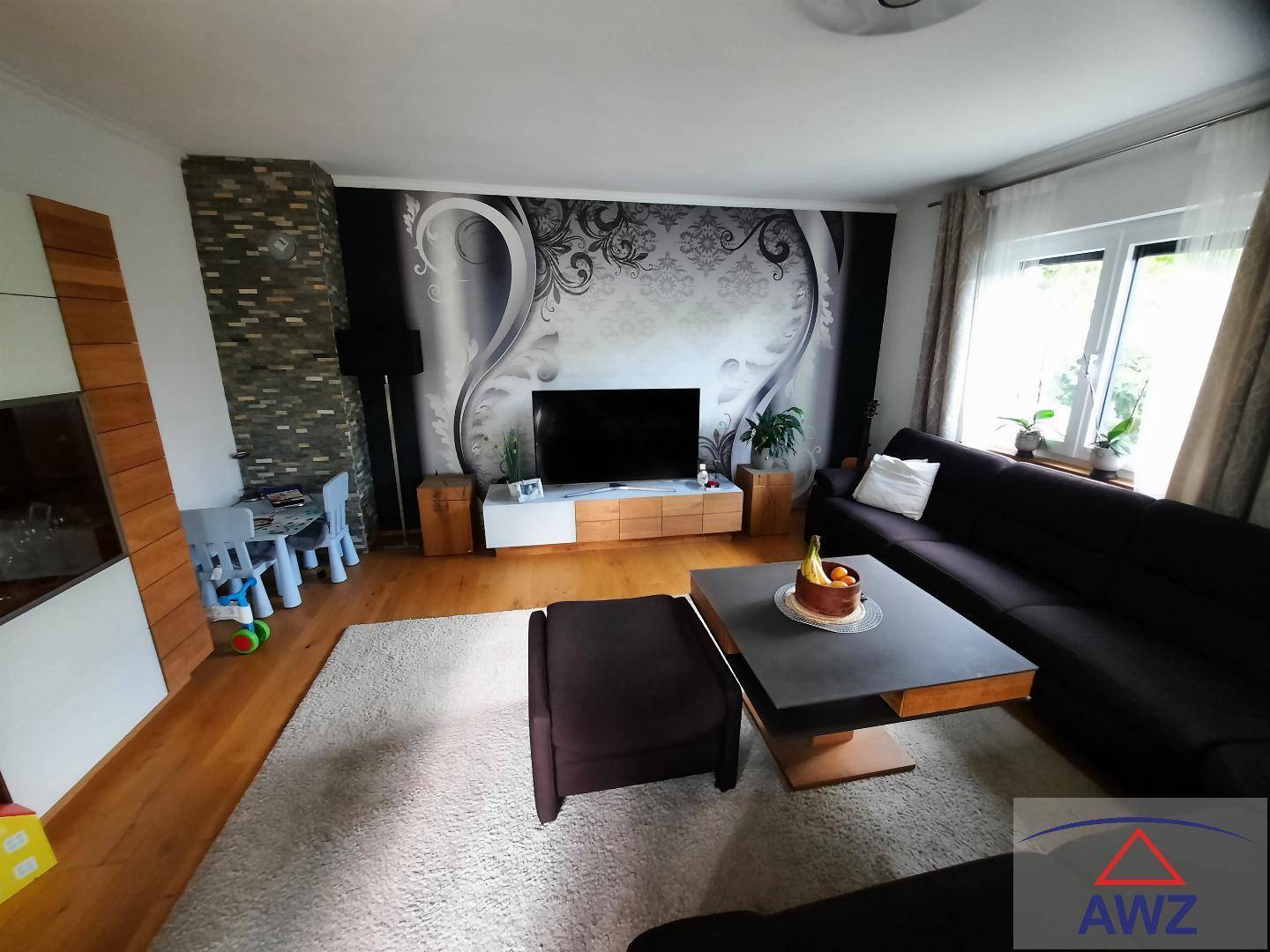 Gemütliches Wohnzimmer mit großem Sofa, dekorativer Tapetenwand und einem steinverkleideten Pfeiler.