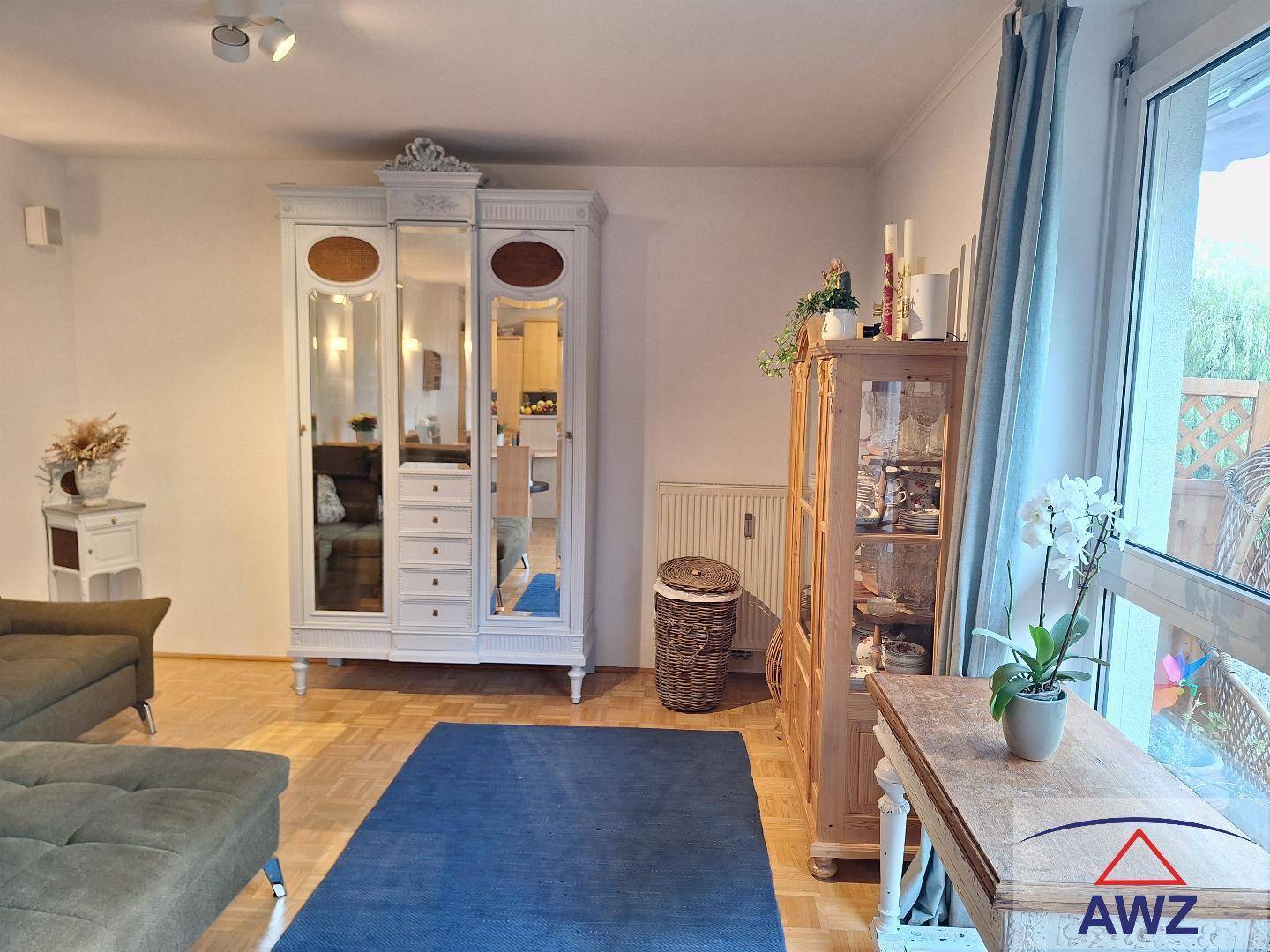 Gemütliches Wohnzimmer mit Parkettboden, großem Fenster und antikem Kleiderschrank.