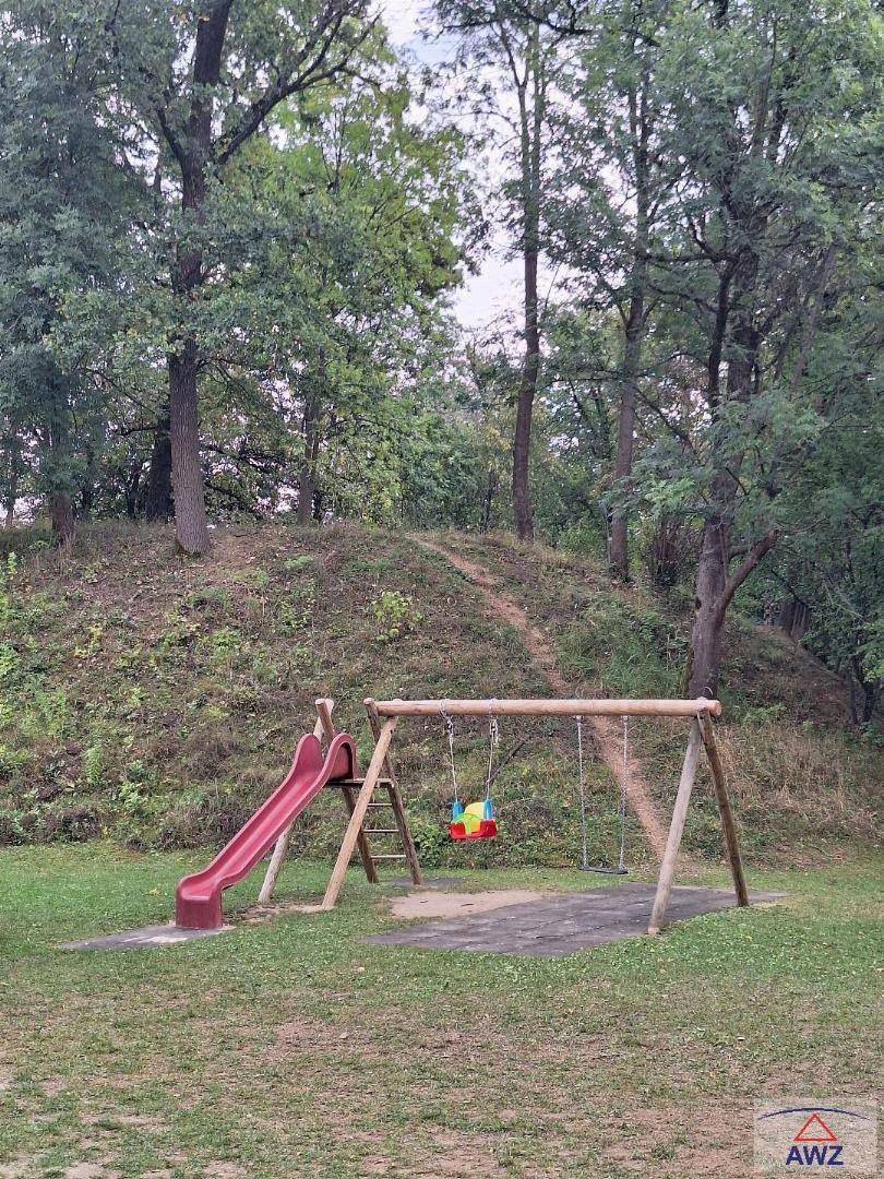 Kinderspielplatz mit Rutsche und Schaukeln in einer grünen, bewaldeten Umgebung.