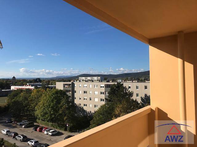 Blick vom Balkon auf umliegende Gebäude, einen Parkplatz und eine weite Landschaft mit Bergen.