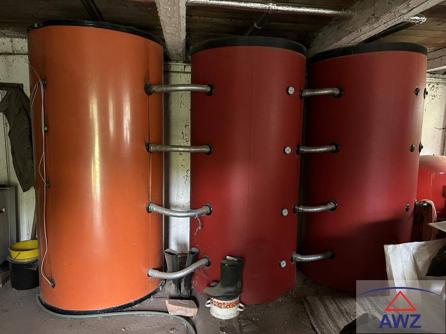 Heizungsraum mit drei großen Warmwasserspeichern und sichtbaren Rohren.